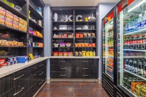 Una despensa bien surtida con diversos alimentos y bebidas, incluyendo aperitivos, conservas y un refrigerador con bebidas.