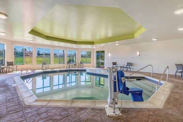 Una piscina interior con paredes de vidrio transparente, un trampolín y un puesto de socorrista.
