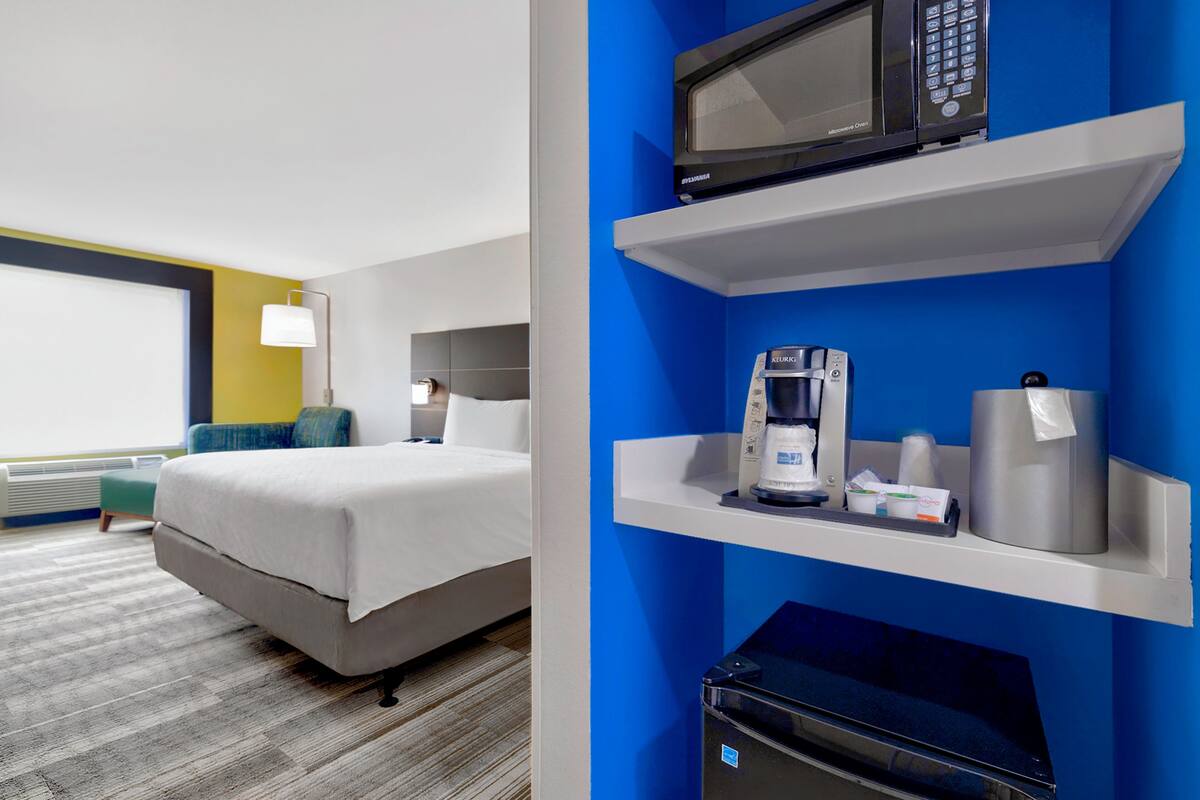 Una habitación de hotel con cama, cafetera, microondas y refrigerador pequeño.