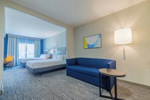 Ein Hotelzimmer mit einem Bett, einem blauen Sofa, einem kleinen Tisch, einer Lampe und einem Gemälde an der Wand.