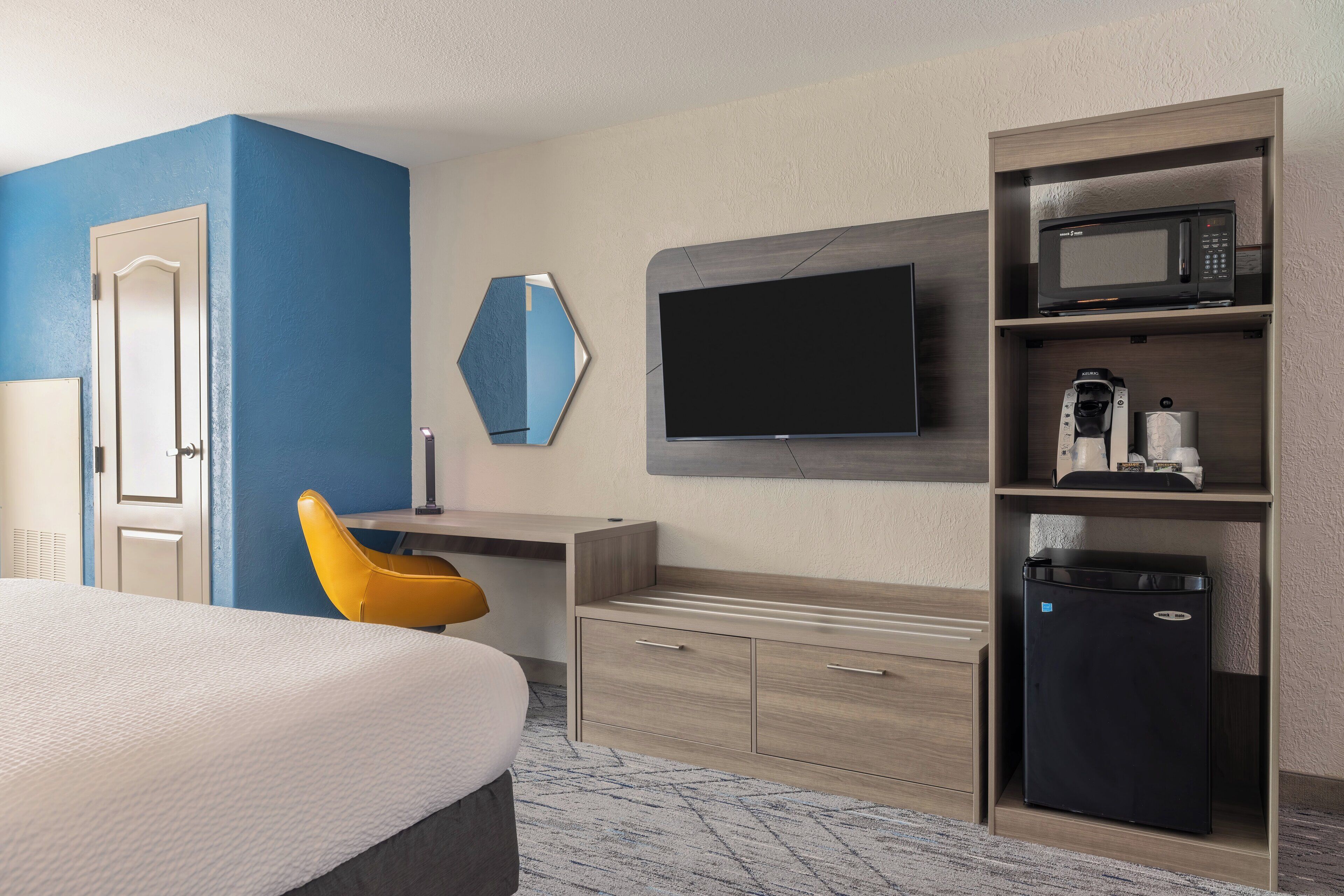 A hotel room with a bed, a desk with a chair, a television, a microwave, and a mini-fridge.