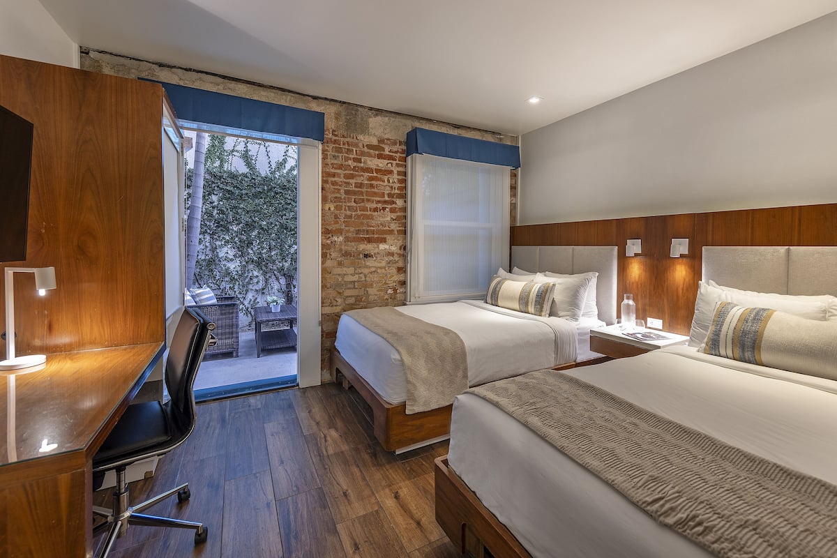 Quarto de hotel com duas camas, uma escrivaninha e vista para o exterior.