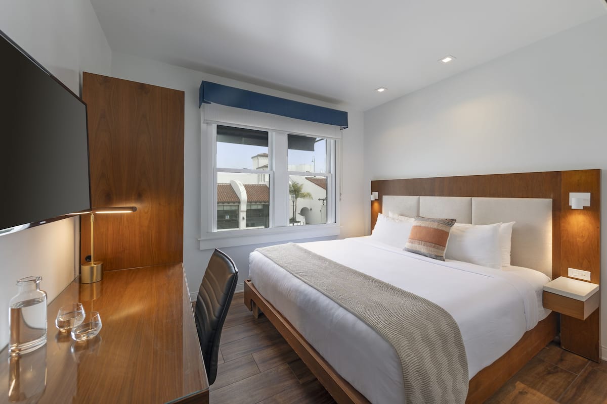 Quarto de hotel moderno com uma cama grande, uma escrivaninha com televisão de tela plana e uma janela com vista para edifícios.