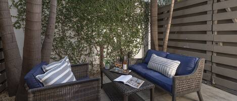 A patio with wicker furniture, a blue sofa, and a small table with a bottle and glass.