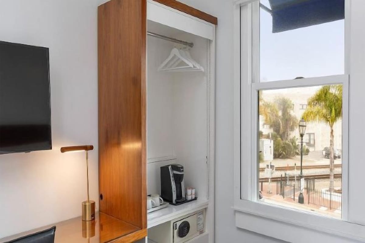 A room with a television, a wooden cabinet, a coffee machine, and a window with a view of the outside.