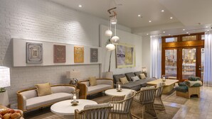 A modern living room with a white brick wall, a sofa set, a coffee table, wicker chairs, and artwork. - Riviera Beach House (Santa Barbara)