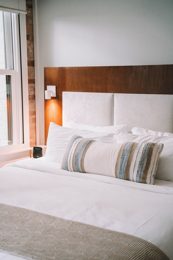A neatly made bed with white linens and a striped throw pillow.