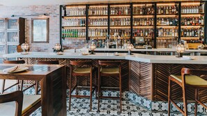 A bar area with a brick wall, shelves of liquor bottles, and bar stools. - Riviera Beach House (Santa Barbara)