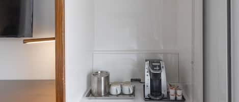 A compact room with a built-in coffee maker, a small shelf with cups, and a control panel.