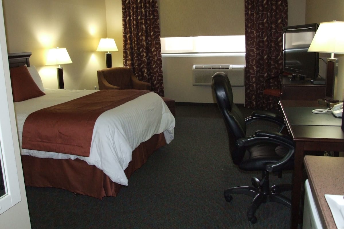 Une chambre d’hôtel comprenant un lit, deux chaises, un bureau avec un ordinateur et une télévision.