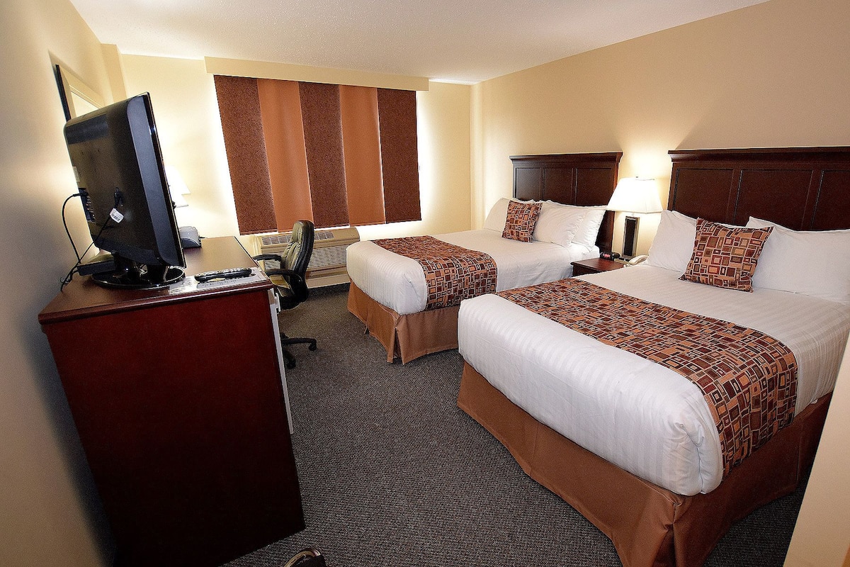 Une chambre d’hôtel avec deux lits, un bureau avec un ordinateur, une chaise et un téléviseur.