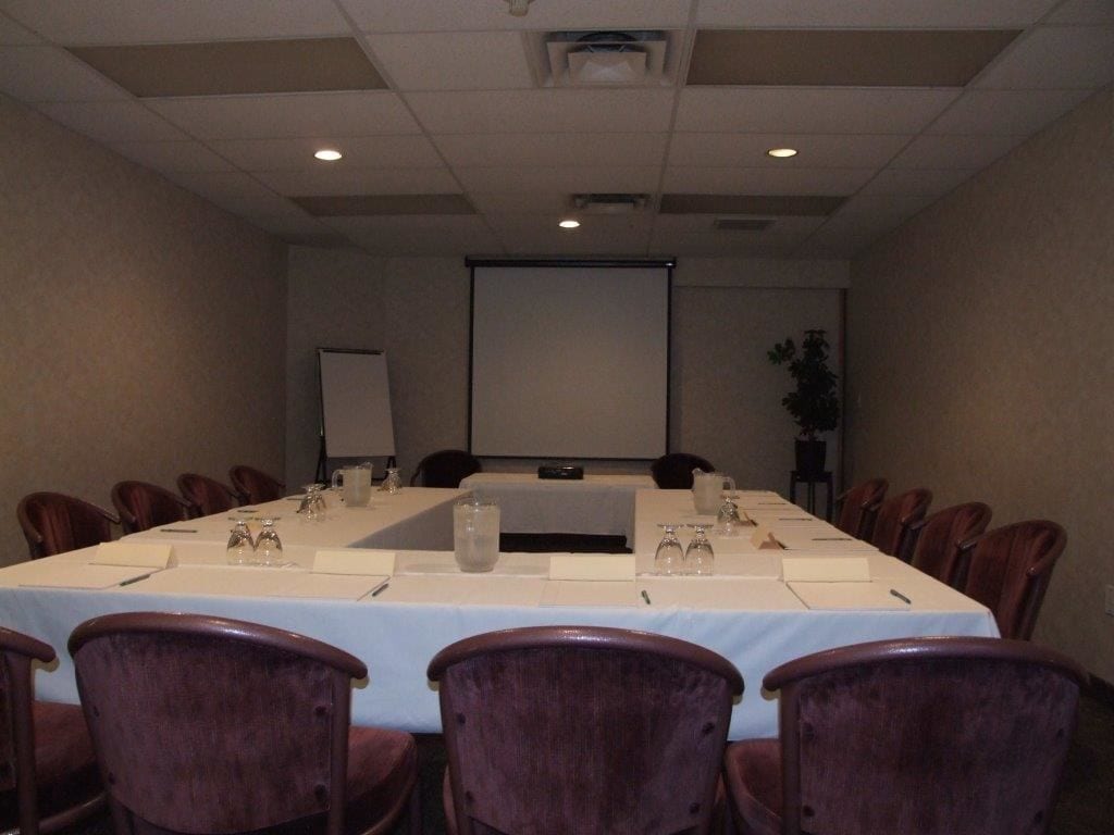 Une salle de conférence équipée d’une longue table, de chaises, d’un écran de projection et d’un tableau blanc.