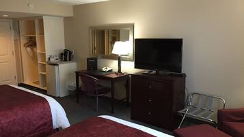 A hotel room with two beds, a desk with a computer, a TV, a chair, a wardrobe, and a small kitchenette.