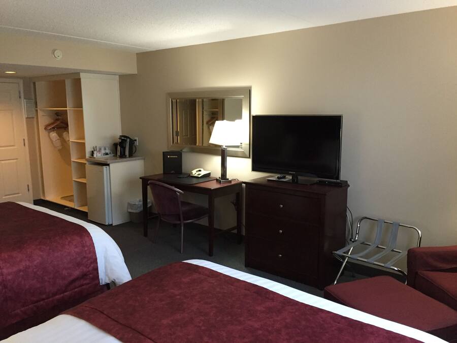 A hotel room with two beds, a desk with a computer, a TV, a chair, a wardrobe, and a small kitchenette.