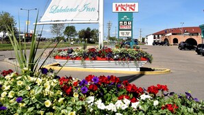Letrero de Lakeland Inn con diseño de vela, cartel de hotel y estacionamiento con macizos de flores de colores.