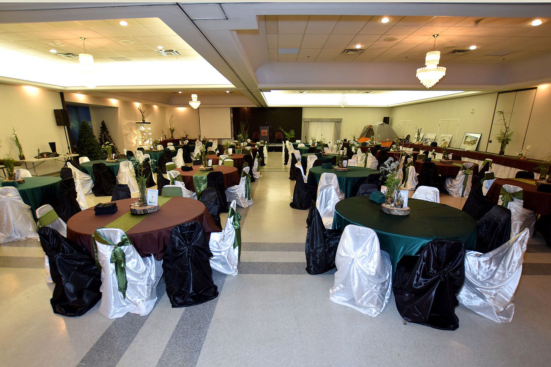 Un salón de banquetes con mesas redondas, cada una cubierta con un mantel verde y cubresillas blancos.