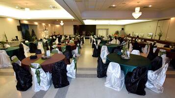 Un salón de banquetes con mesas redondas, cada una cubierta con un mantel verde y cubresillas blancos.