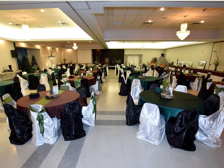 Un salón de banquetes con mesas redondas, cada una cubierta con un mantel verde y cubresillas blancos.