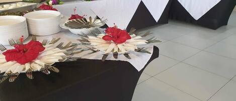 Montaje tipo bufé con varias estaciones de servicio, incluyendo tazones y platos para comida, y una pieza central decorativa con flores rojas.