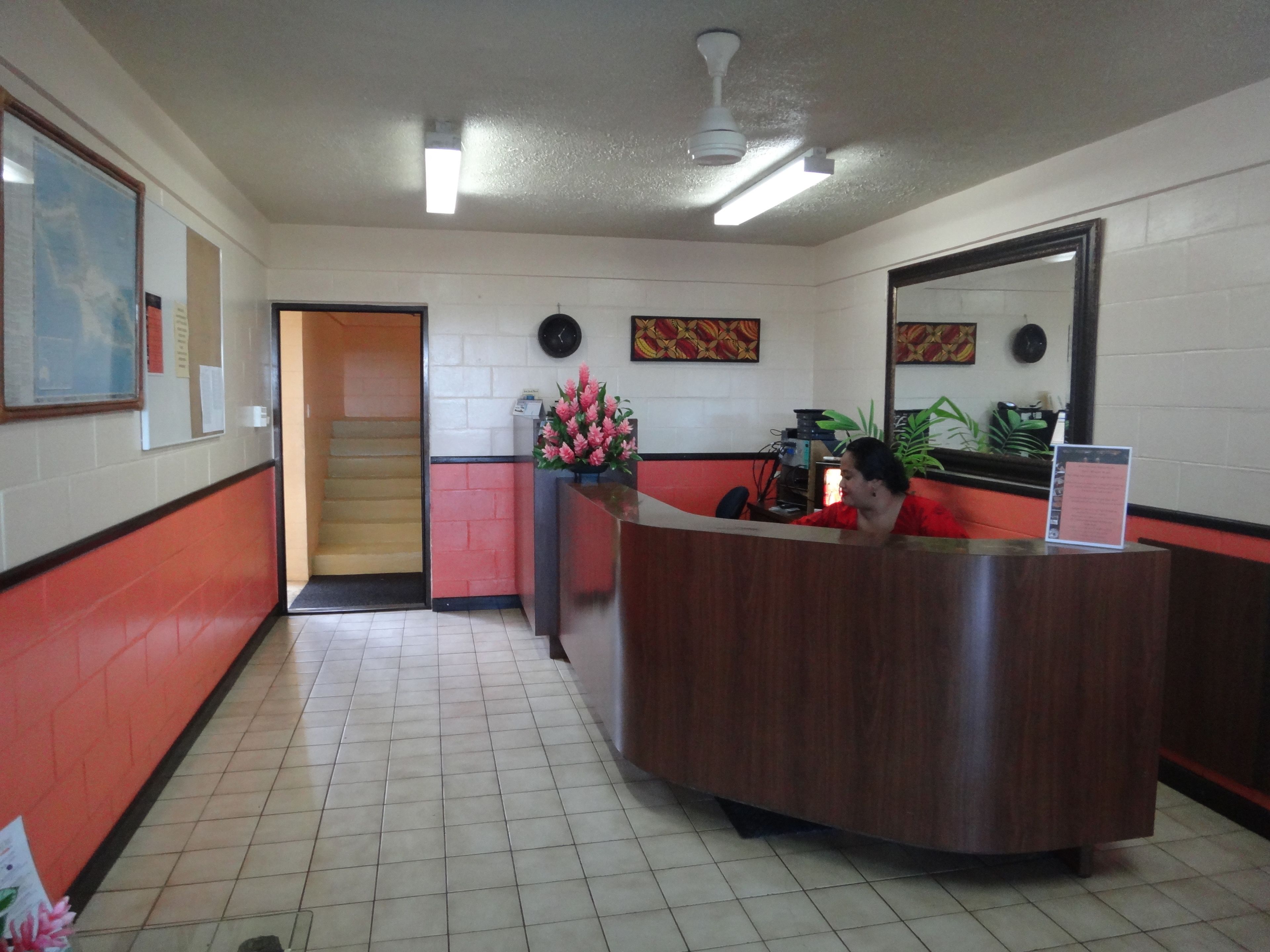 A reception area with a wooden reception desk, a clock on the wall, a staircase, and a plant.