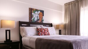 A hotel room with a bed, two bedside lamps, a painting on the wall, and a window with curtains.