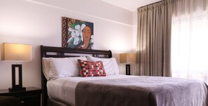 A hotel room with a bed, two bedside lamps, a painting on the wall, and a window with curtains.