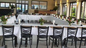A long dining table with white tablecloths and black chairs, set up in a spacious room with large windows and a modern ceiling design. - Insel Fehmarn Hotel (Apia)