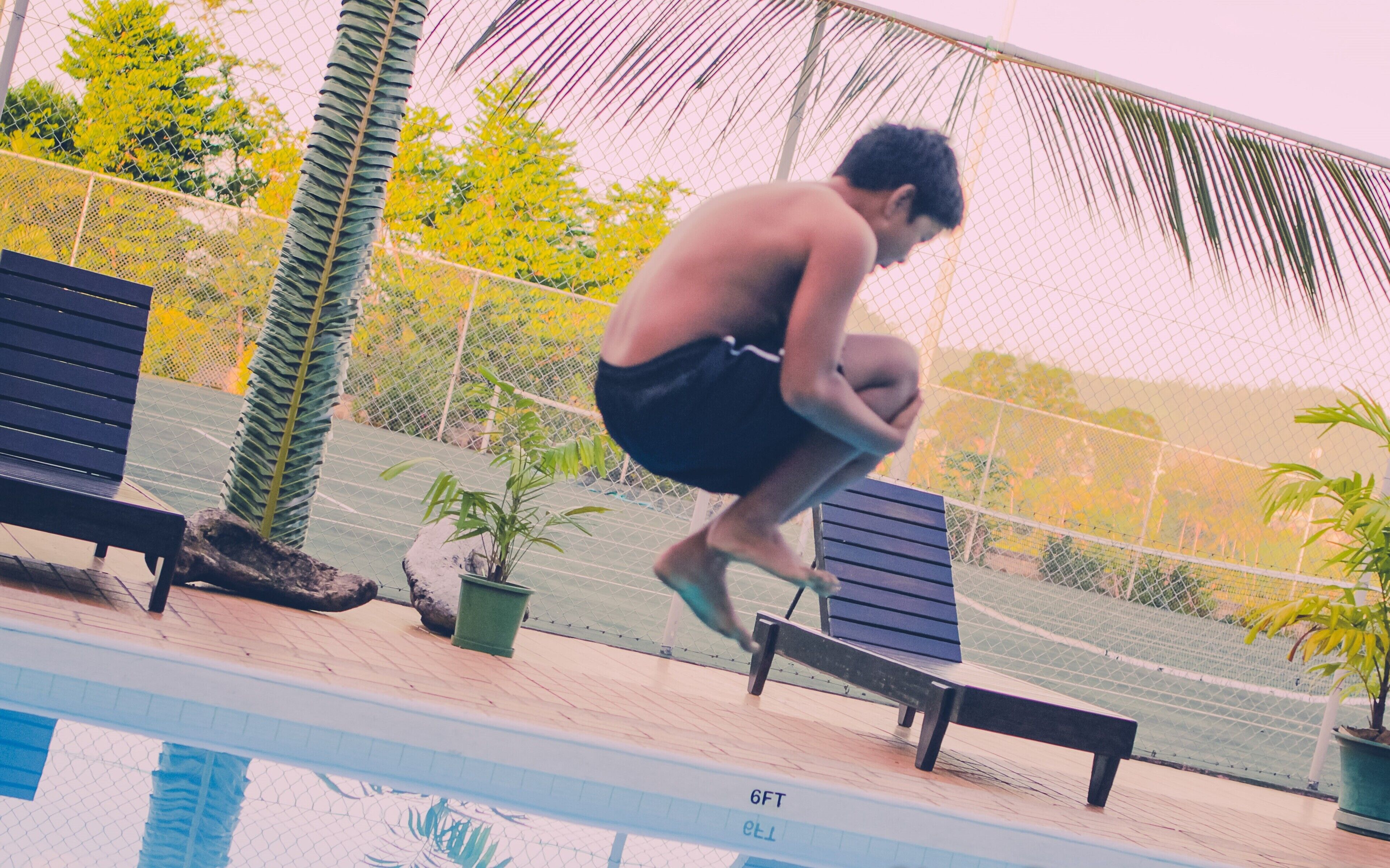 Una persona salta a una piscina con una cerca y bancos alrededor.