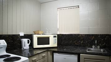 Una cocina compacta con estufa blanca, microondas, cafetera y pileta.