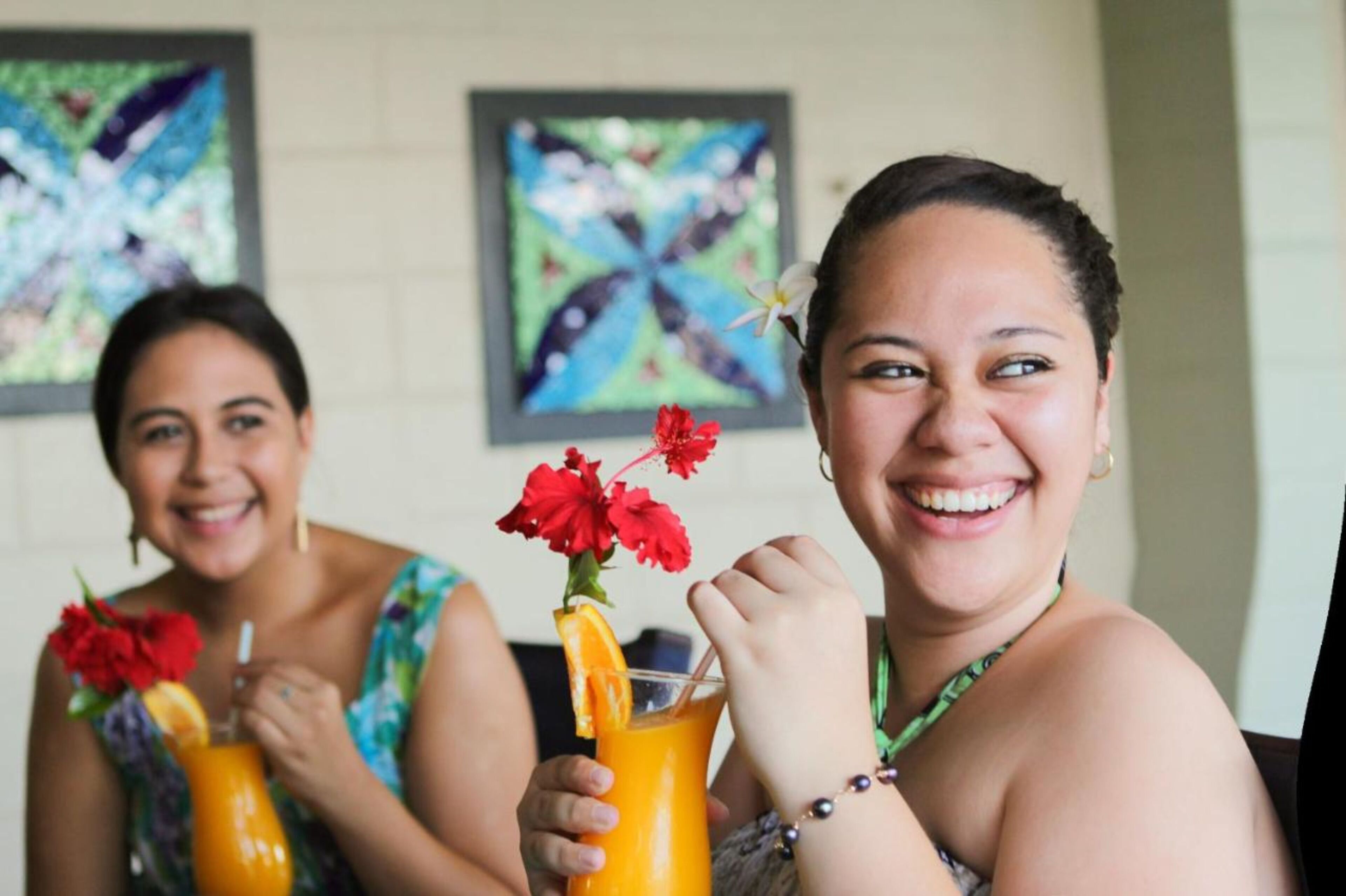 Two people holding drinks with flowers, in a room with abstract art on the wall.