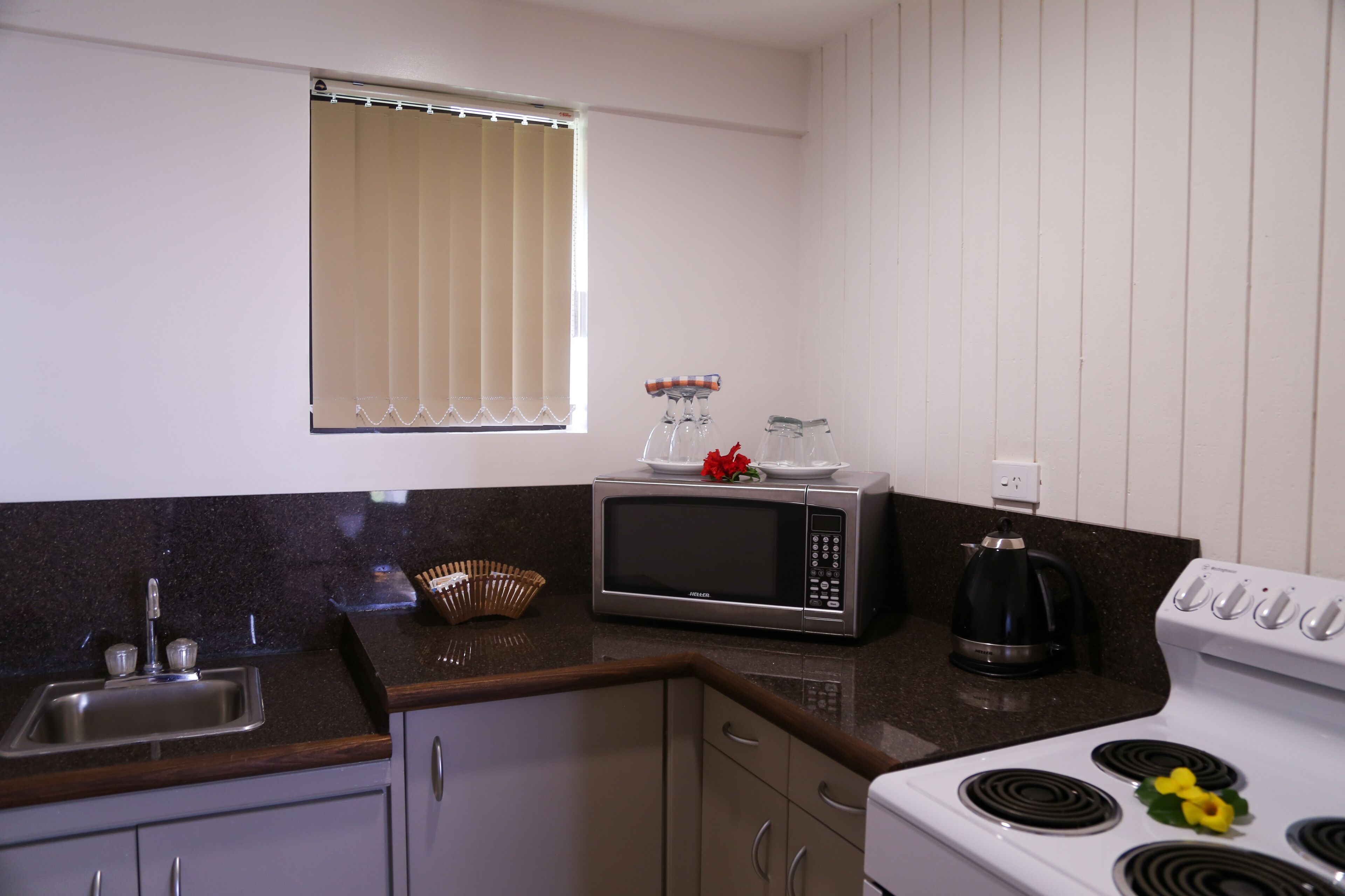 Cocina equipada con lavamanos, microondas, estufa y ventana con persianas.