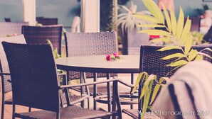 An outdoor seating area with wicker chairs and tables, some with flowers. - Insel Fehmarn Hotel (Apia)