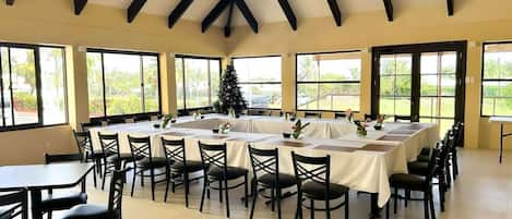 A conference room with a high ceiling and large windows, tables set for a meeting, and a Christmas tree.