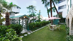 A well-maintained garden with a gazebo, a seating area with a striped umbrella, and a stone pathway.