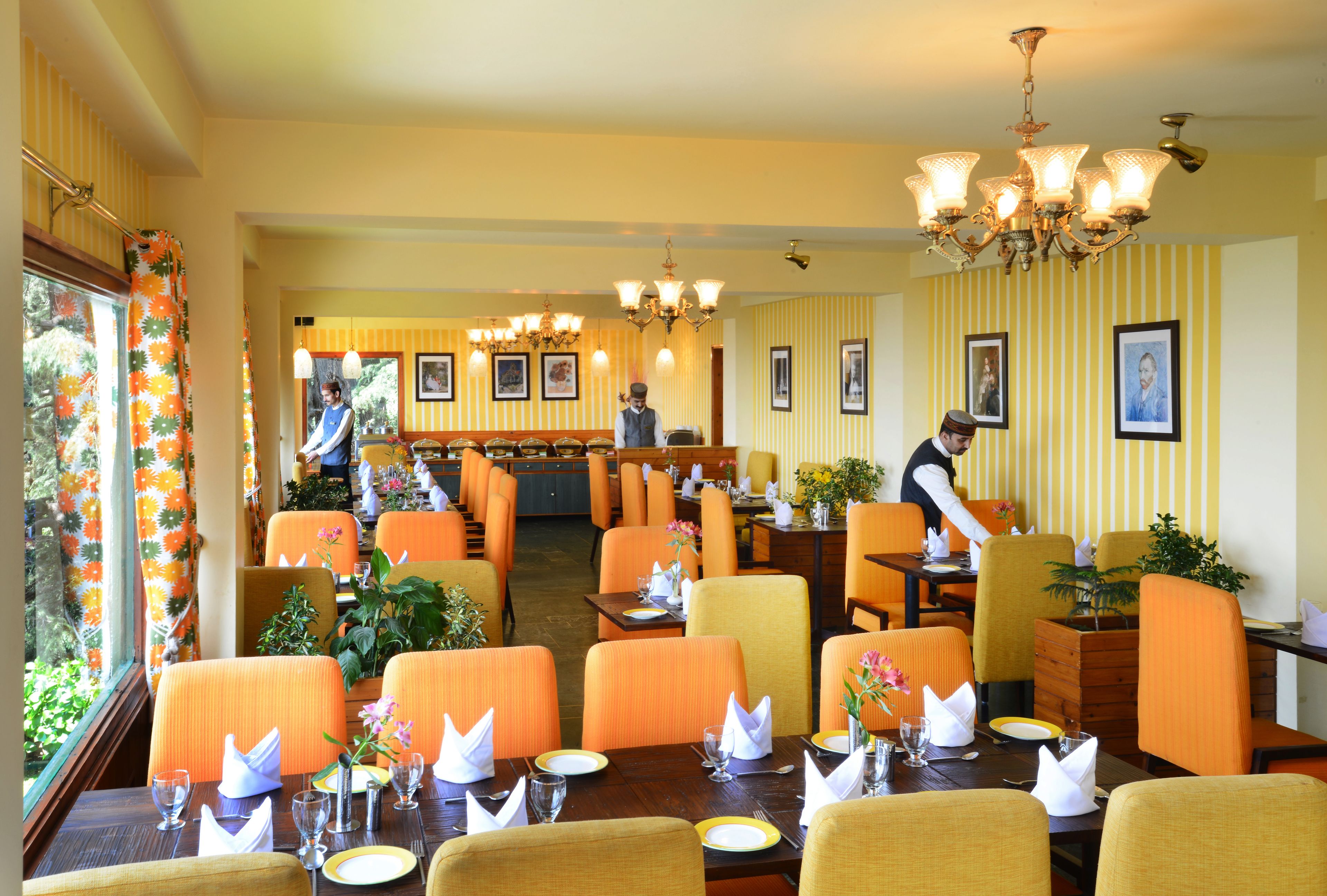 A restaurant with orange chairs, wooden tables, and chandeliers.