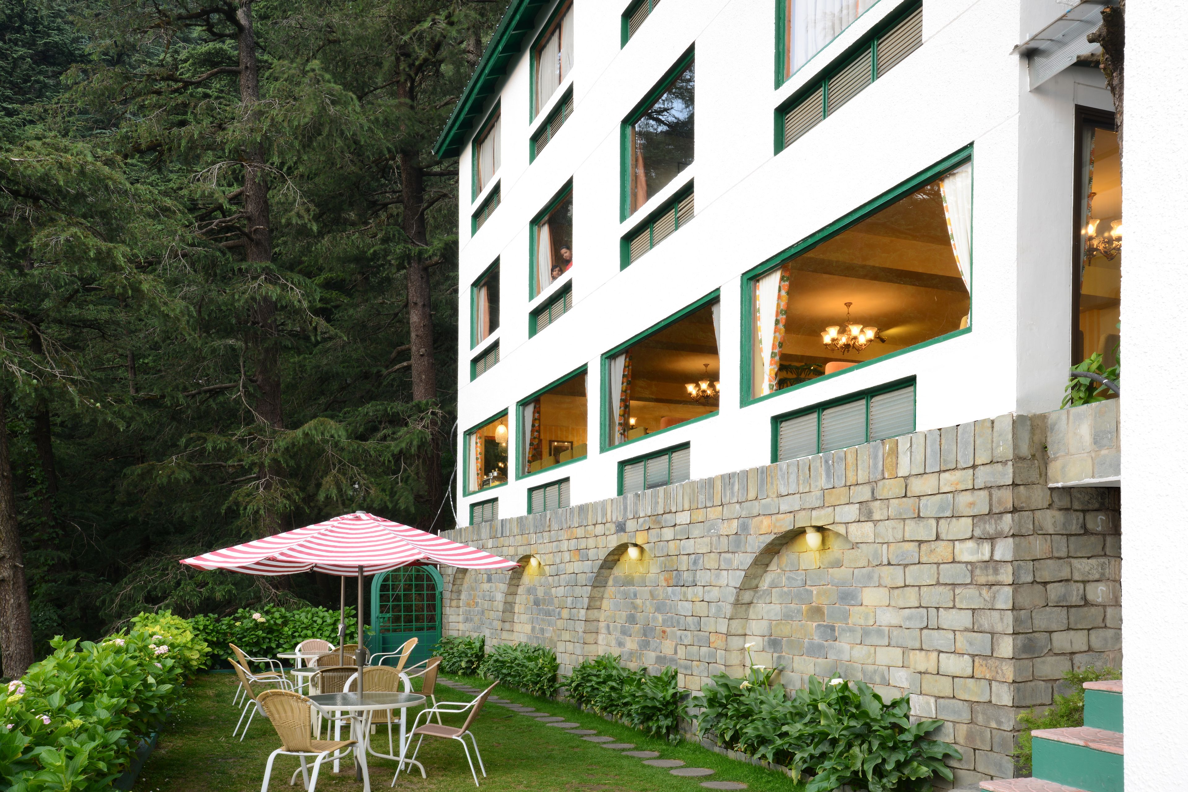 A building with multiple windows, a stone wall, and a patio with chairs and an umbrella.