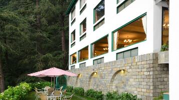 A building with multiple windows, a stone wall, and a patio with chairs and an umbrella.
