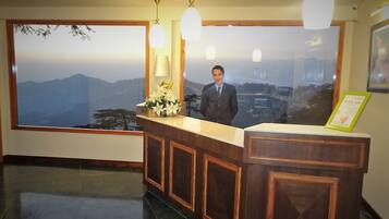 A reception desk with a view of mountains through a large window, a man standing behind it, and a framed sign on the counter.