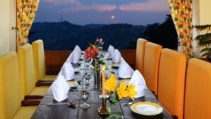 A dining table set for two with a view of a sunset over a cityscape.