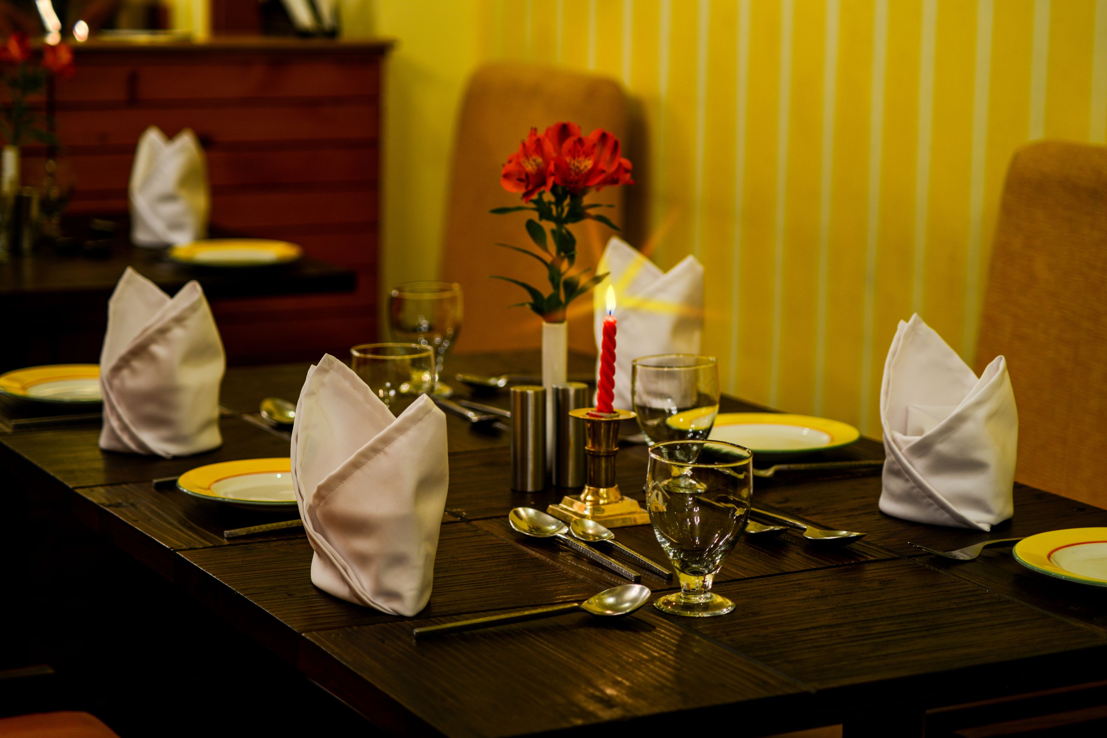 A dining table set with white napkins, plates, cutlery, and a candle.