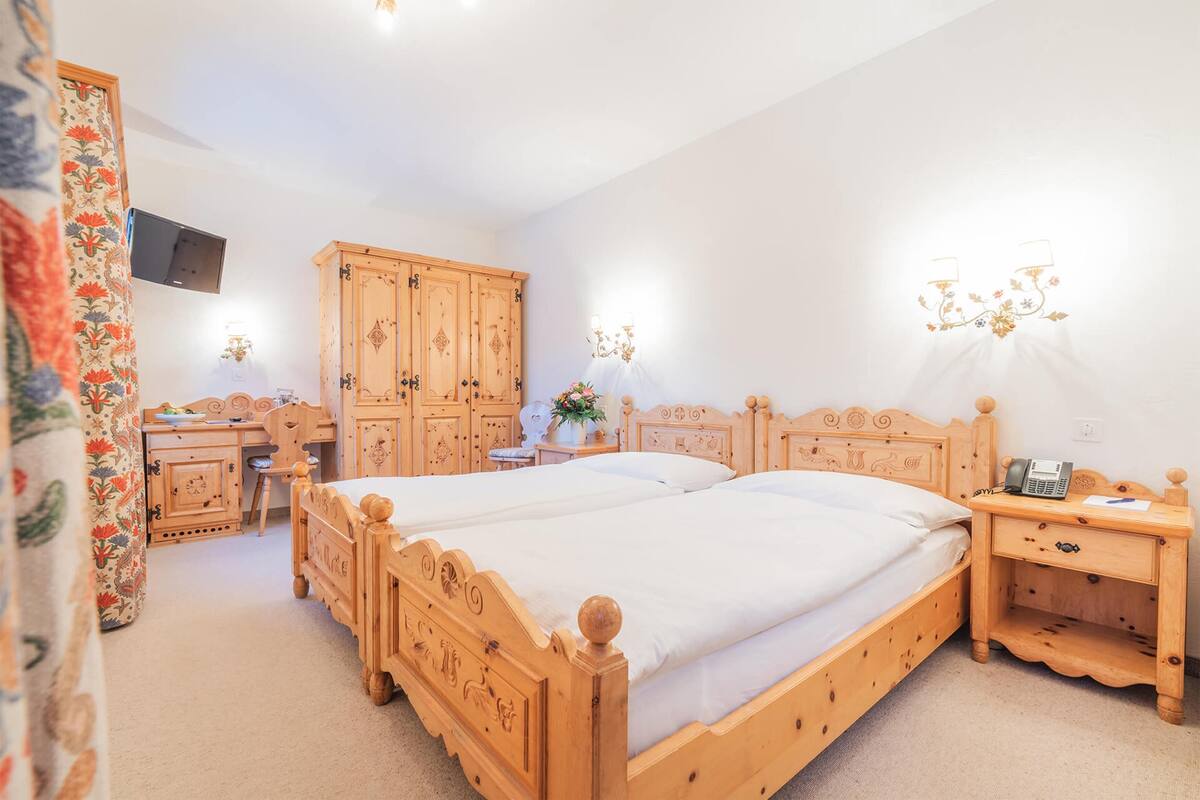 Une chambre à coucher avec deux lits en bois, un bureau, une armoire et une table de chevet avec une lampe.