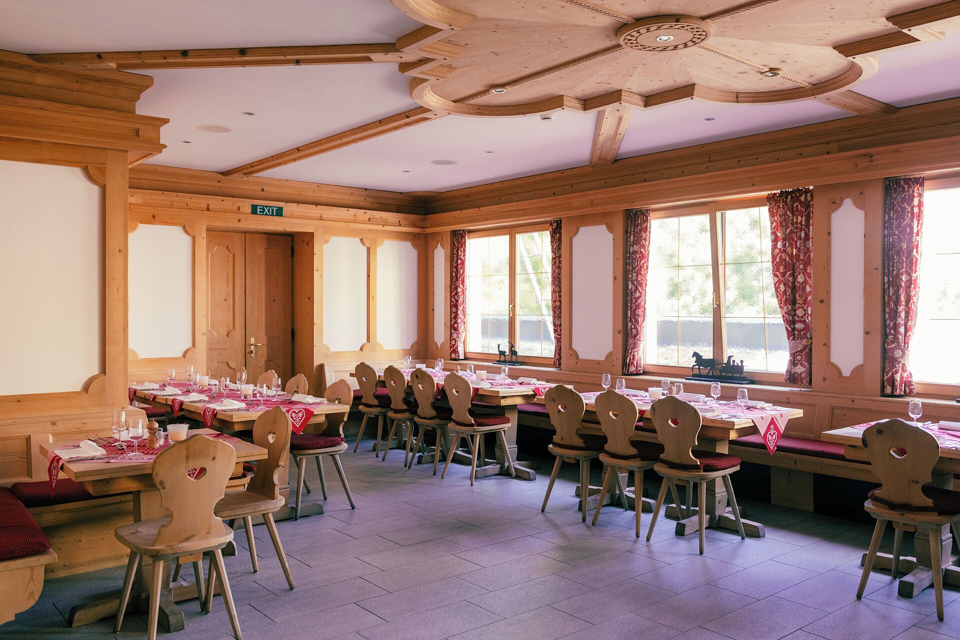Un comedor con mesas y sillas de madera, ventanas amplias y un ventilador de techo.
