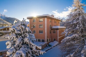 Un edificio de varios pisos con árboles cubiertos de nieve y montañas al fondo.