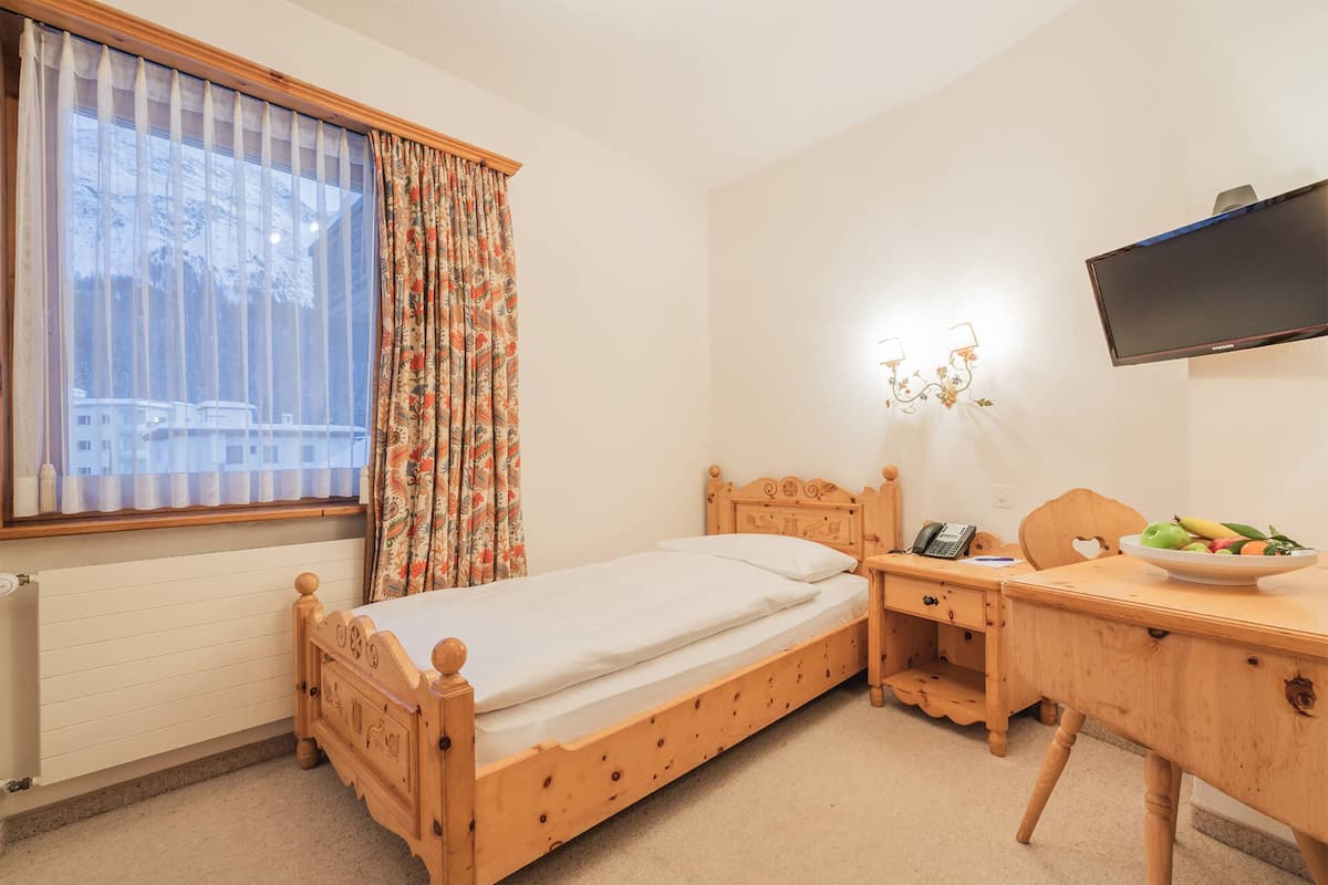 Une chambre à coucher avec un lit en bois, un bureau, une chaise, une télévision et une fenêtre avec des rideaux.