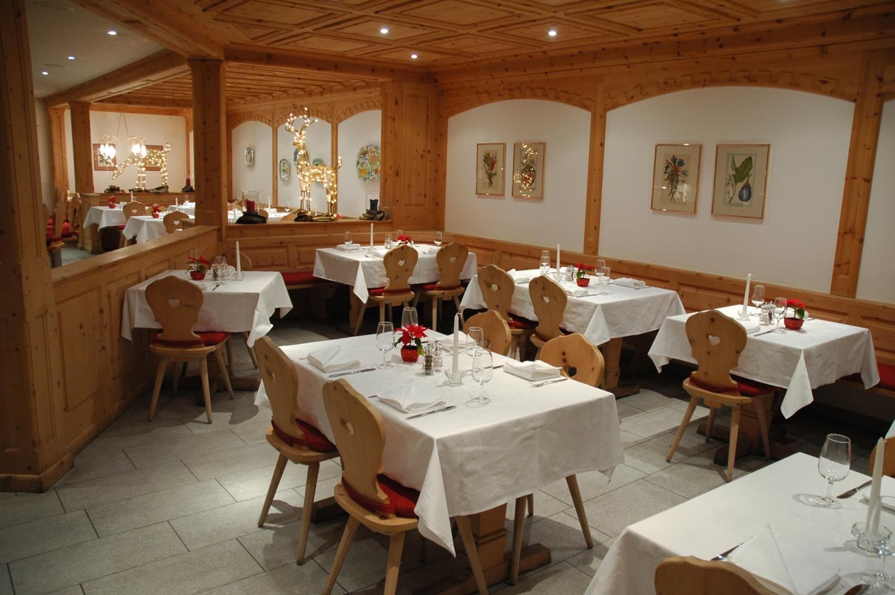 Ein Restaurant mit Holzeinrichtung, mehreren Tischen mit weißen Tischdecken und Stühlen.
