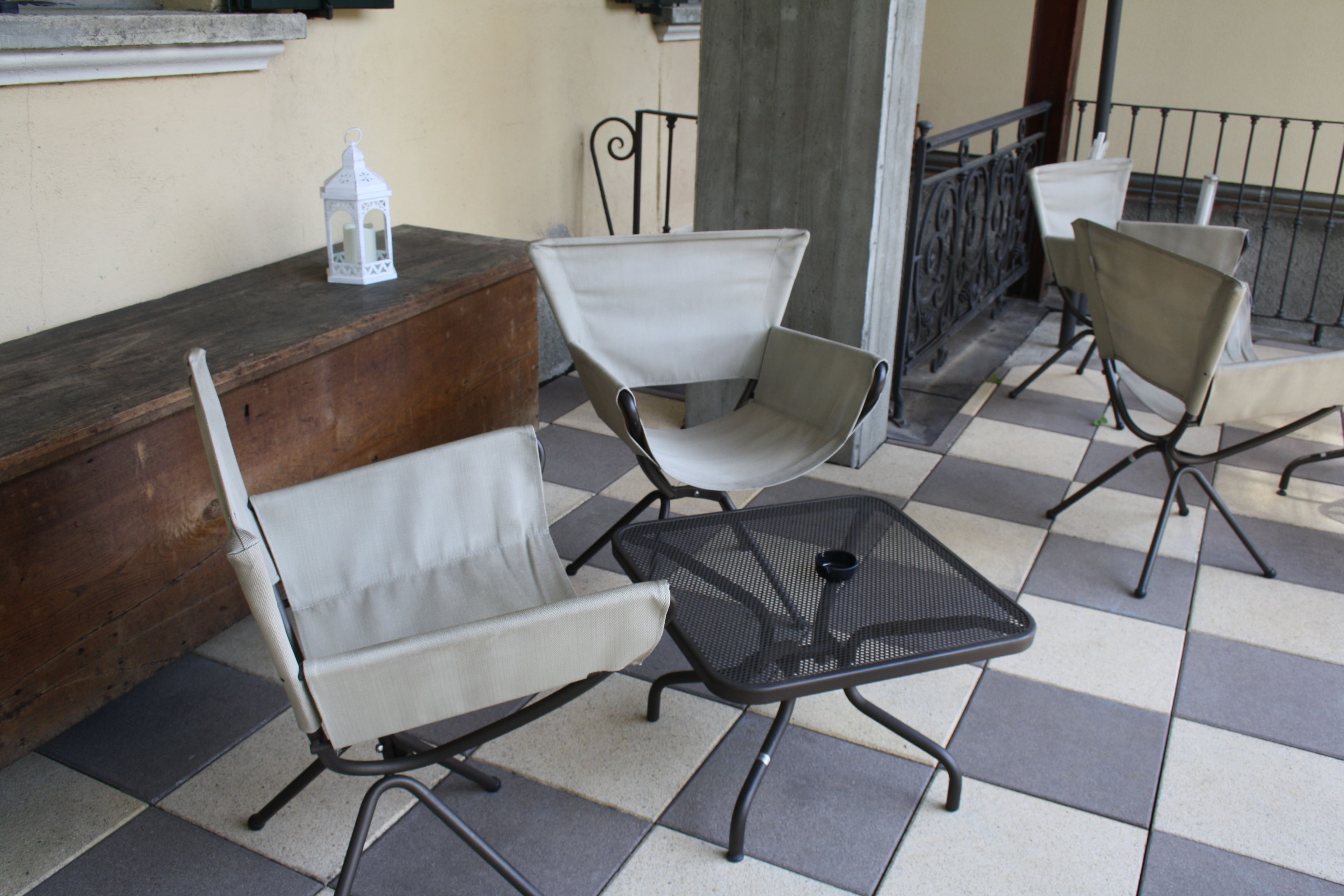Eine Terrasse mit Schachbrettboden, Metalltischen und weißen Sitzgelegenheiten mit Kissen.