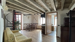 Amplia sala de estar con techo de madera, un sofá, una mesa de comedor y una escalera que sube a otro nivel.