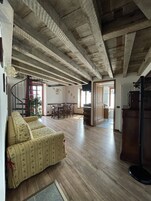A spacious living area with a wooden ceiling, a sofa, a dining table, and a staircase leading to another level.