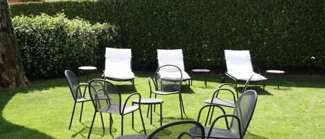 A patio with several chairs and tables, surrounded by well-maintained grass and a hedge.