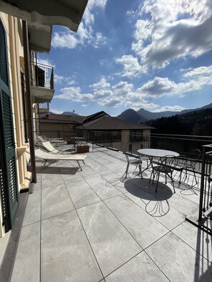 A rooftop terrace with a view of mountains, featuring outdoor seating and a tiled floor. - Albergo La Torre (Centro Valle Intelvi)